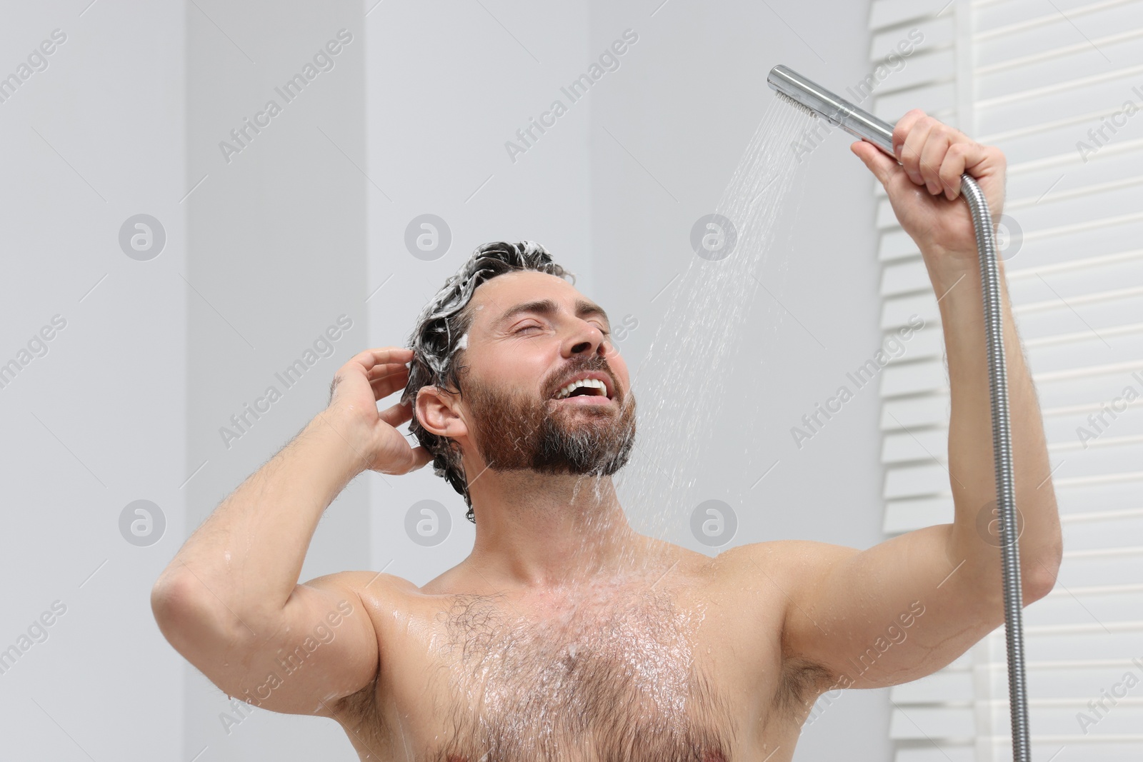 Photo of Happy man washing his hair with shampoo in shower