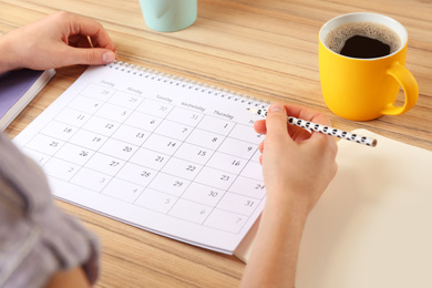 Photo of Woman with calendar at wooden table in office, closeup