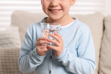 Little girl holding glass of fresh water indoors, closeup