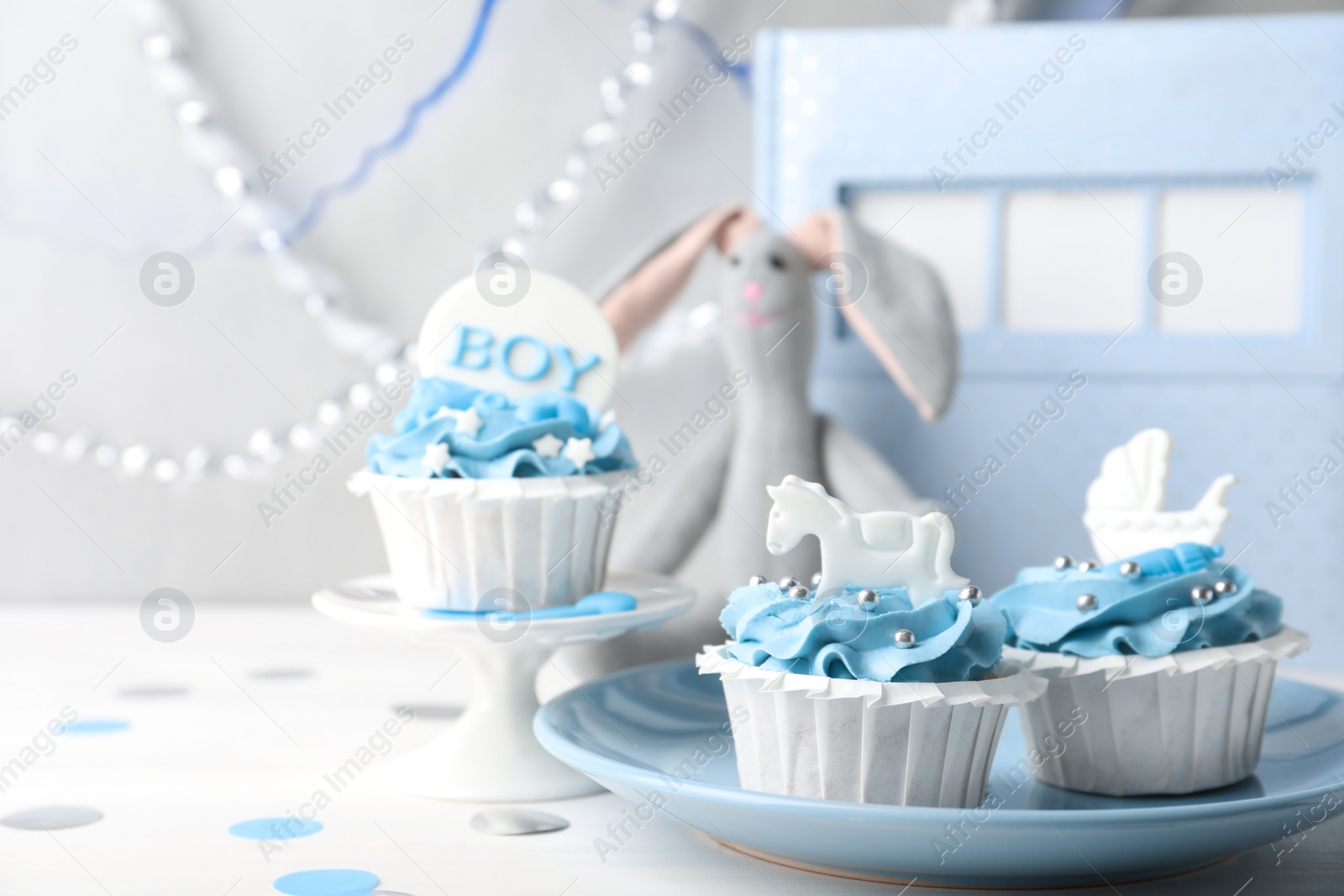 Photo of Delicious cupcakes with light blue cream and toppers for baby shower on white wooden table