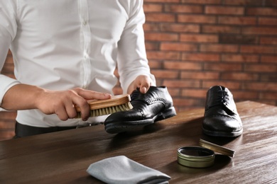 Man cleaning leather shoe at wooden table indoors, closeup