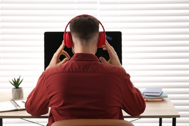 Man in headphones studying on computer indoors, back view. Online translation course
