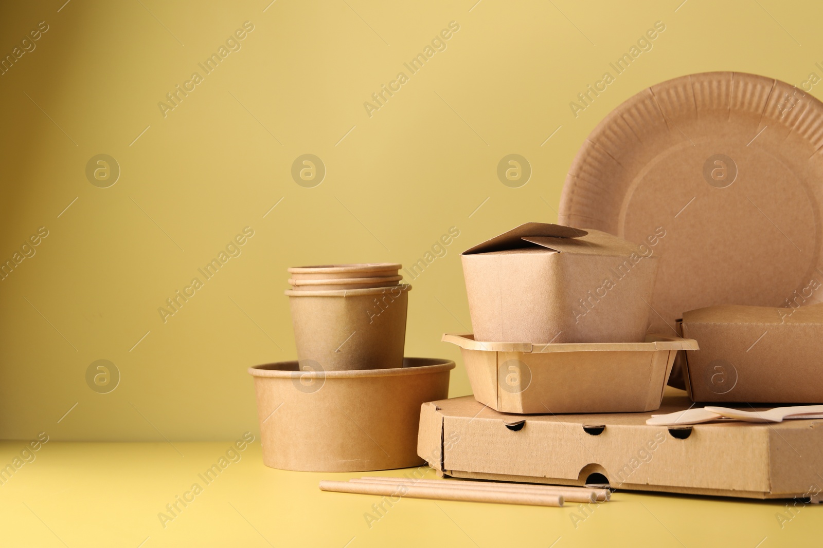 Photo of Eco friendly food packaging. Paper containers and tableware on pale yellow background, space for text