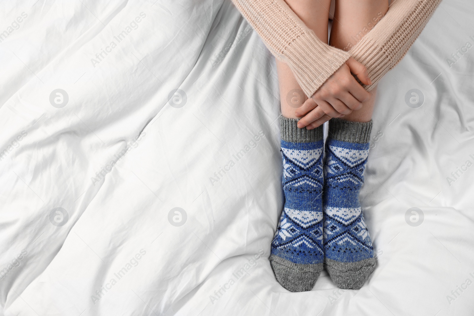 Photo of Woman wearing knitted socks on white fabric, top view. Warm clothes