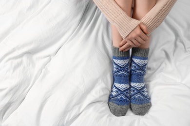 Photo of Woman wearing knitted socks on white fabric, top view. Warm clothes