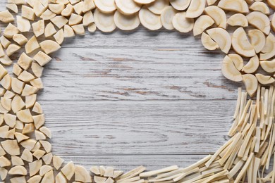 Frame of cut fresh ripe parsnips on white wooden table, flat lay. Space for text