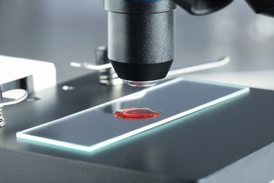 Photo of Glass slide with sample of red liquid under microscope in laboratory, closeup