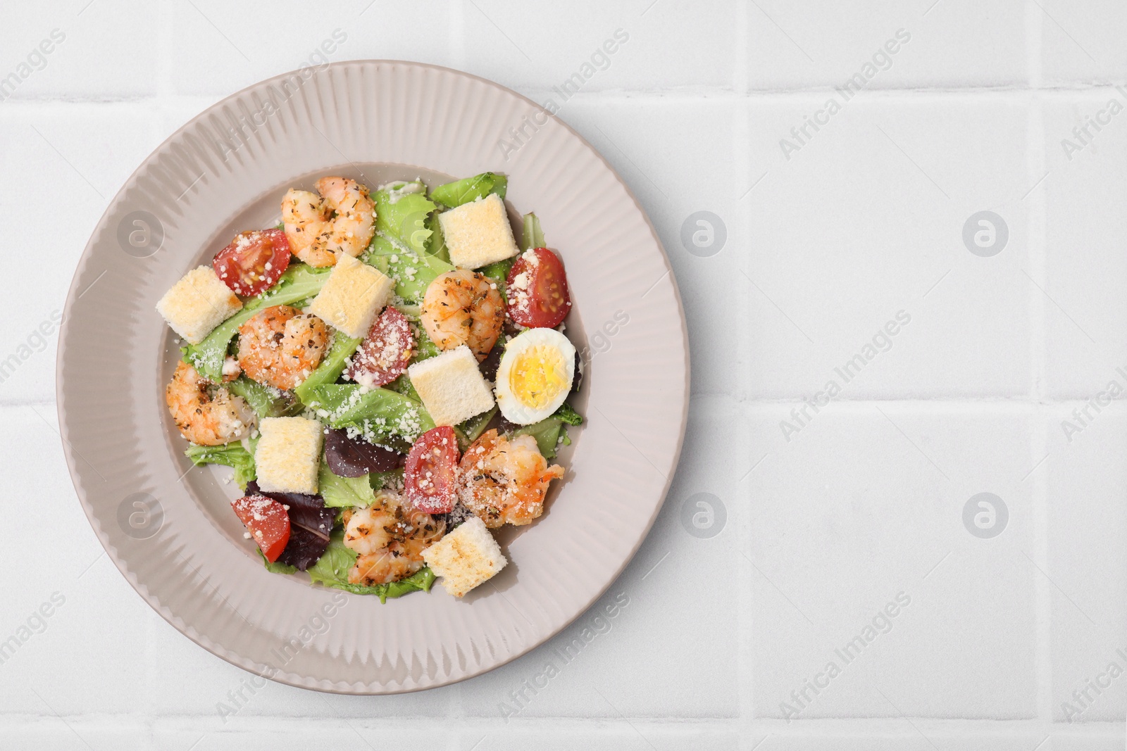 Photo of Delicious Caesar salad with shrimps on white tiled table, top view. Space for text