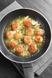 Photo of Delicious scallops with sauce in frying pan on dark gray textured table, top view