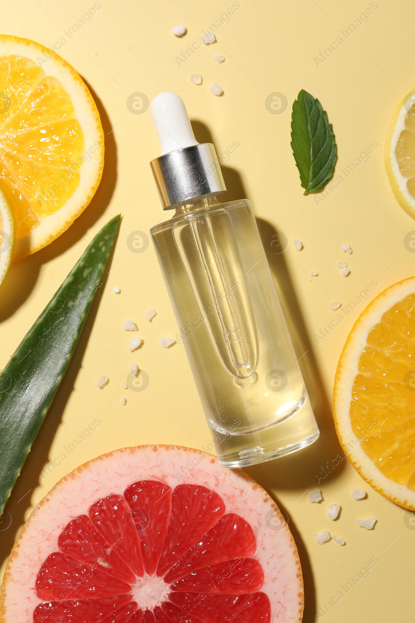 Photo of Bottle of cosmetic serum, sliced citrus fruits and aloe vera leaf on yellow background, flat lay