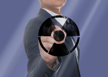 Woman drawing radiation warning symbol with marker on glass board against steel blue background, closeup