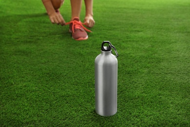 Photo of Bottle of water and blurred woman in sneakers on background, space for text. Fitness equipment