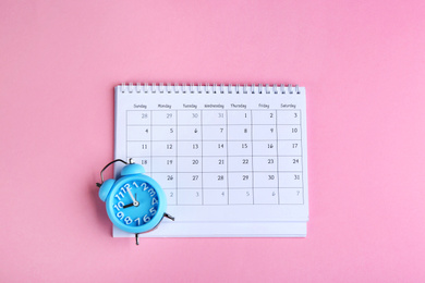Photo of Calendar and alarm clock on pink background, flat lay