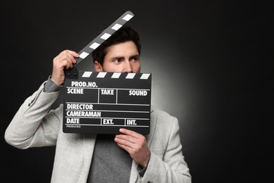 Adult actor holding clapperboard on black background, space for text