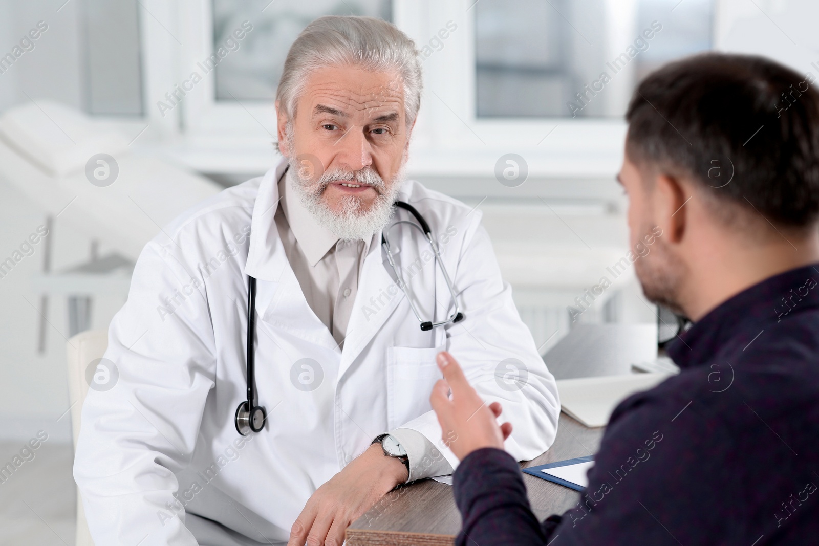 Photo of Senior doctor consulting patient at wooden table in clinic