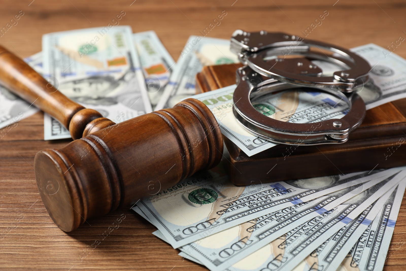 Photo of Judge's gavel, money and handcuffs on wooden table, closeup