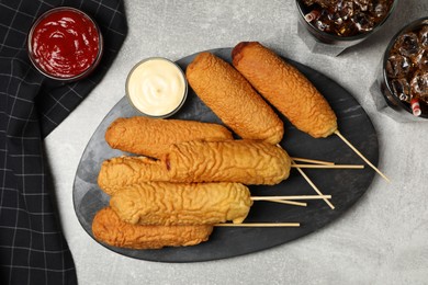 Photo of Delicious deep fried corn dogs with board and sauces on light grey table, flat lay