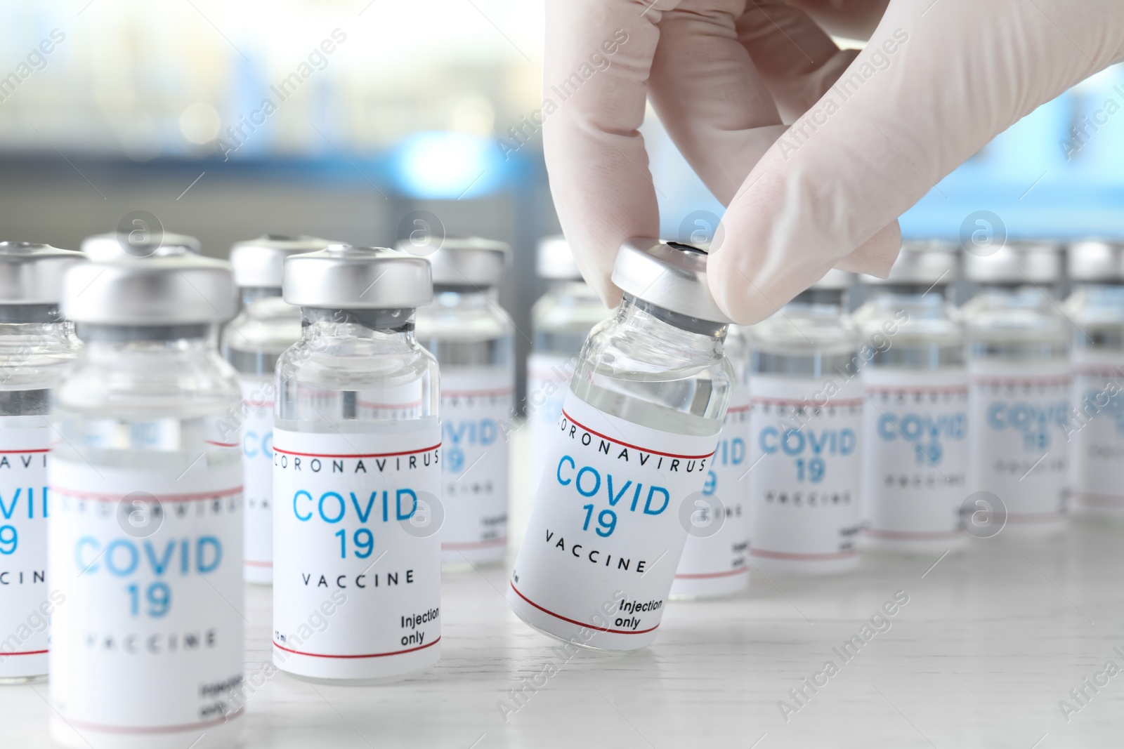 Photo of Doctor taking glass vial with COVID-19 vaccine from  table, closeup