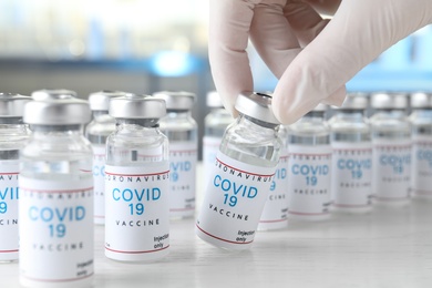 Photo of Doctor taking glass vial with COVID-19 vaccine from  table, closeup