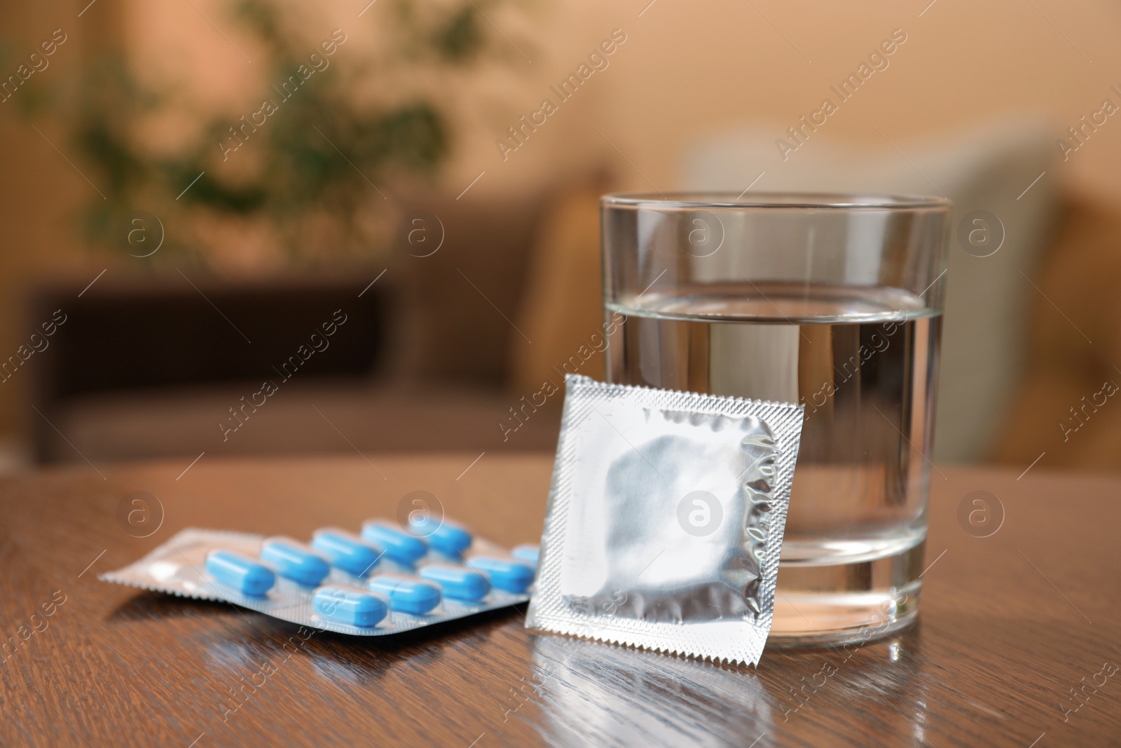 Photo of Glass of water, condoms and pills on wooden table indoors, space for text. Potency problem concept