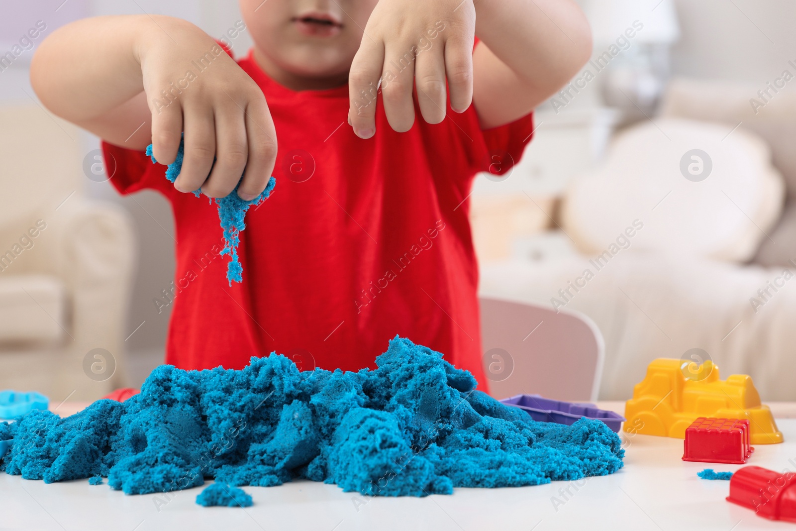 Photo of Little boy playing with bright kinetic sand at table indoors, closeup