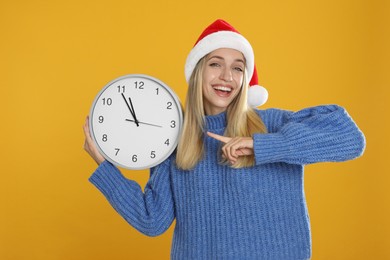 Woman in Santa hat with clock on yellow background. New Year countdown