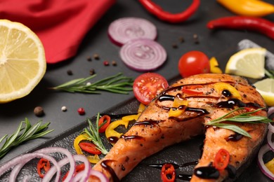 Photo of Slate plate with tasty salmon steak and vegetables on black table, closeup