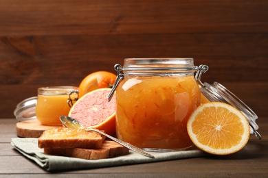 Photo of Delicious orange marmalade, fresh fruits and toasts on wooden table