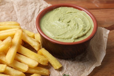 Photo of Parchment with french fries and avocado dip on wooden table, closeup