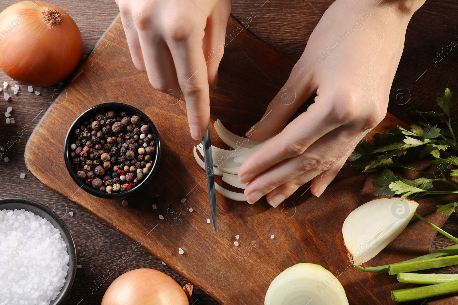 Photo of Woman cutting ripe onion at wooden table, top view