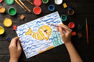 Photo of Girl painting picture of fish on table, top view