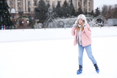 Happy woman skating along ice rink outdoors. Space for text