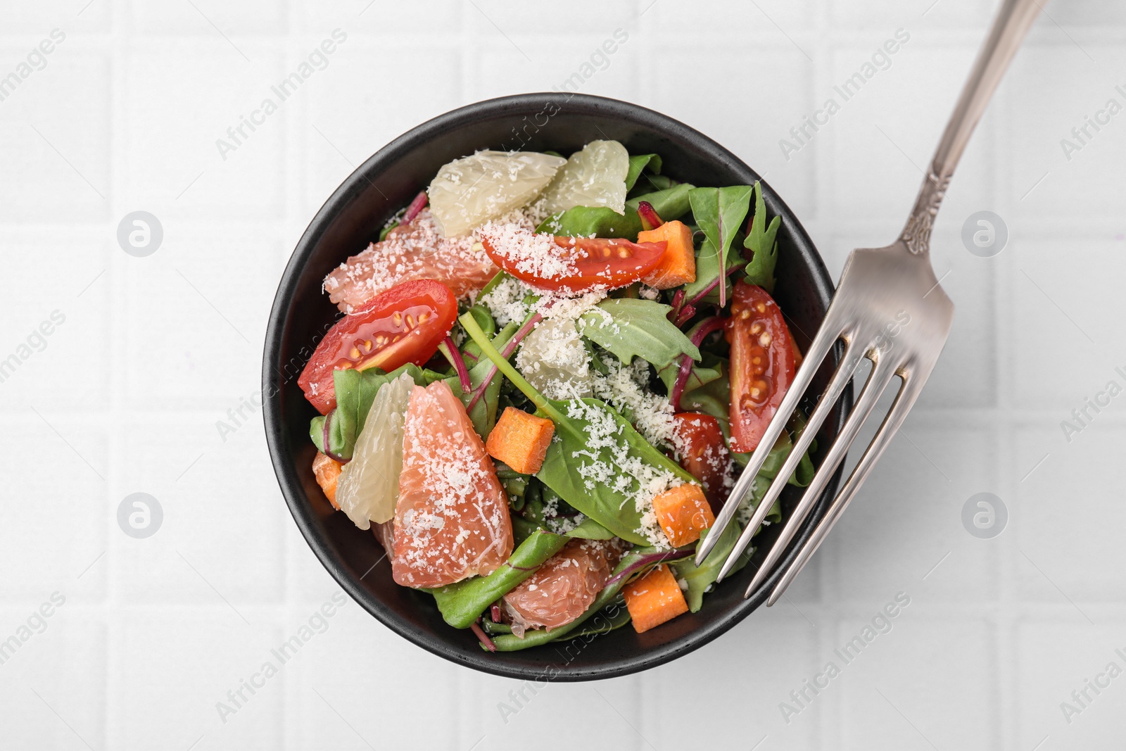 Photo of Delicious salad with pomelo, tomatoes and cheese on white tiled table, top view