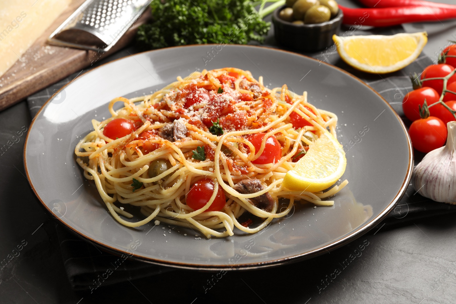 Photo of Delicious pasta with anchovies, tomatoes and parmesan cheese on black table, closeup