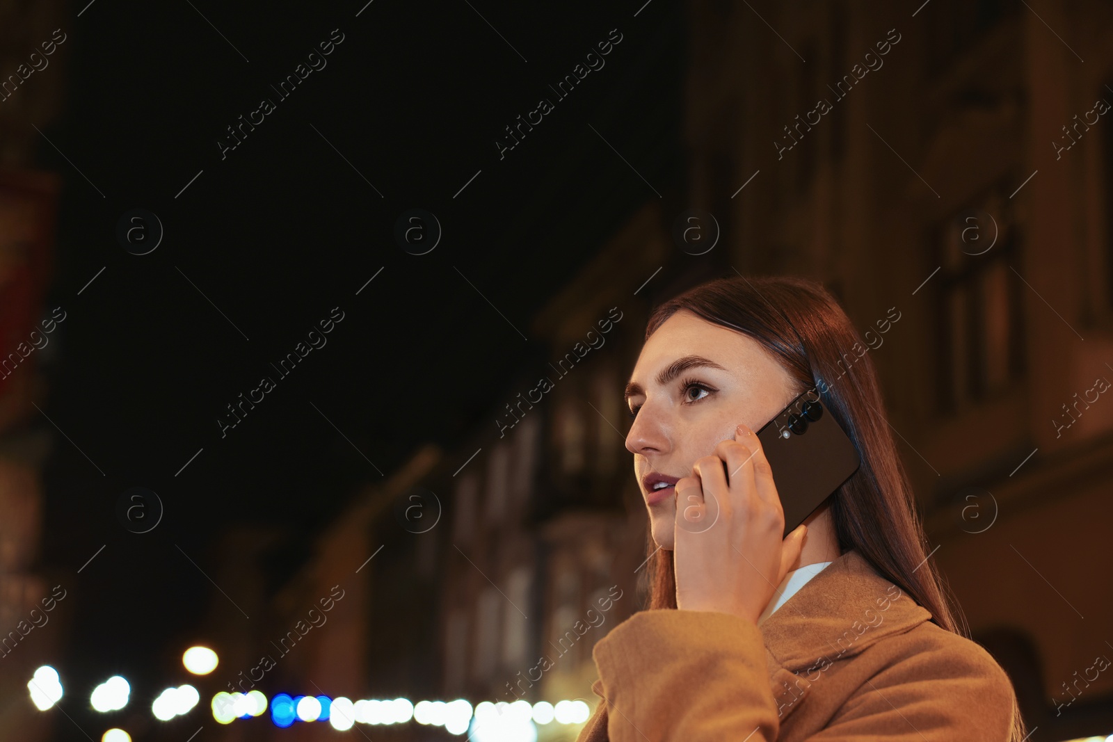 Photo of Beautiful woman talking by smartphone on night city street. Space for text