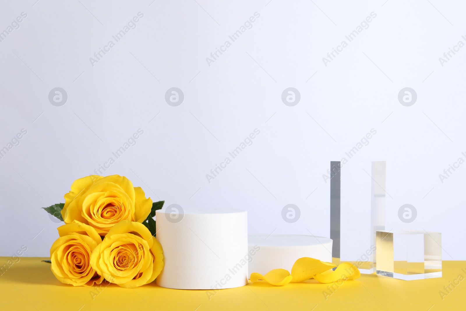 Photo of Beautiful presentation for product. Geometric figures and roses on yellow table against white background, space for text