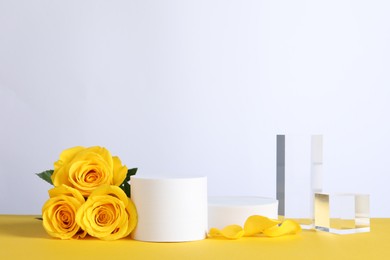 Photo of Beautiful presentation for product. Geometric figures and roses on yellow table against white background, space for text