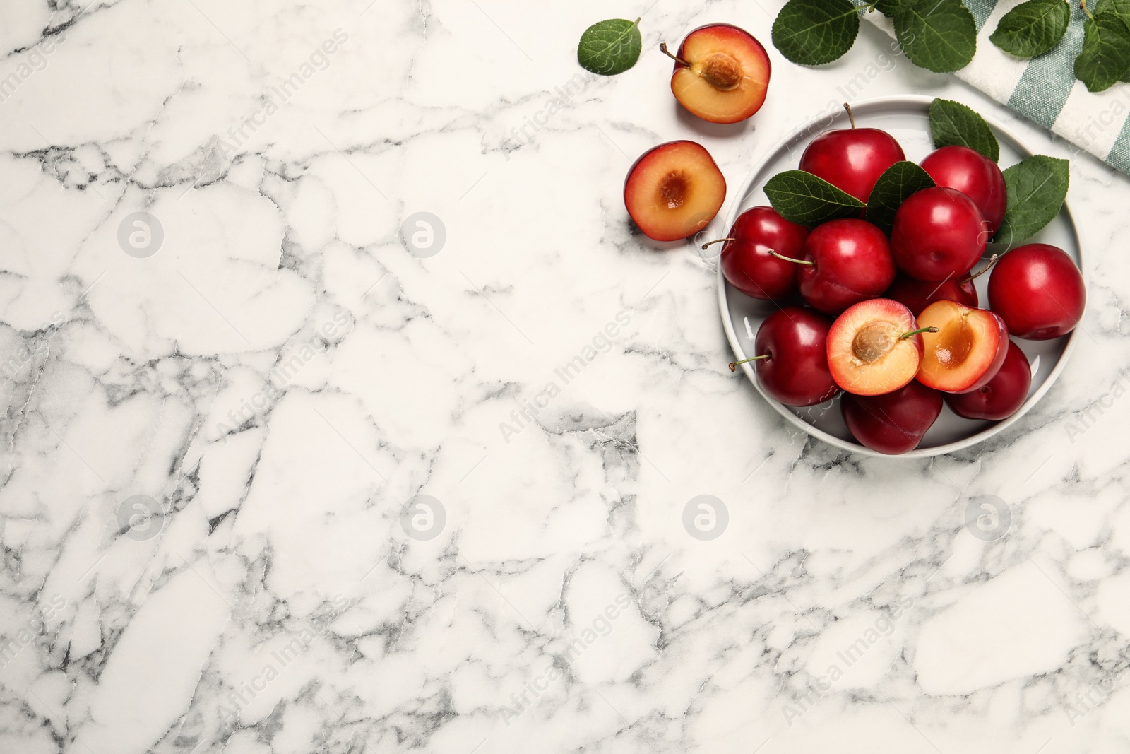 Photo of Delicious ripe cherry plums with leaves on white marble table, flat lay. Space for text