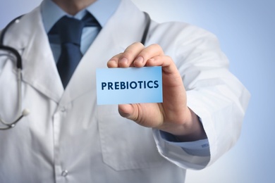 Doctor holding card with word PREBIOTICS on light blue background, closeup