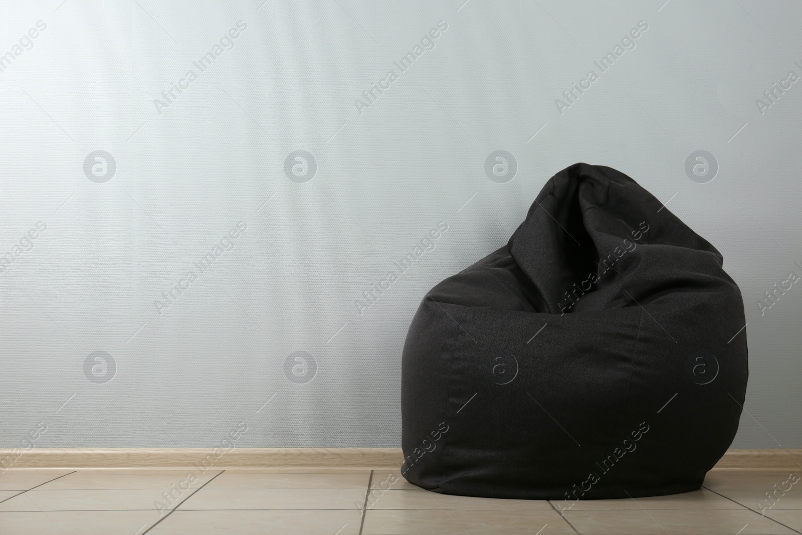 Photo of Black bean bag chair near light grey wall. Space for text