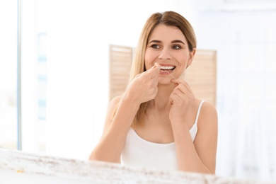 Photo of Young woman flossing her teeth in bathroom