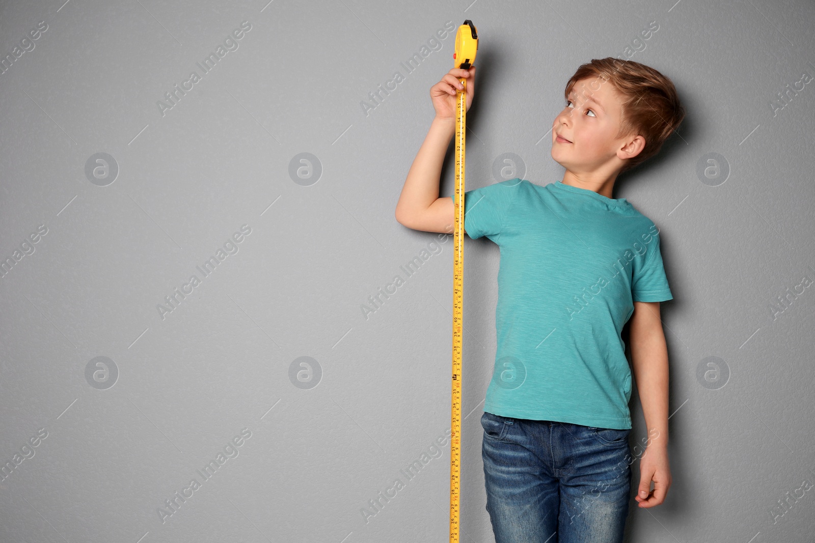 Photo of Little boy measuring his height on grey background