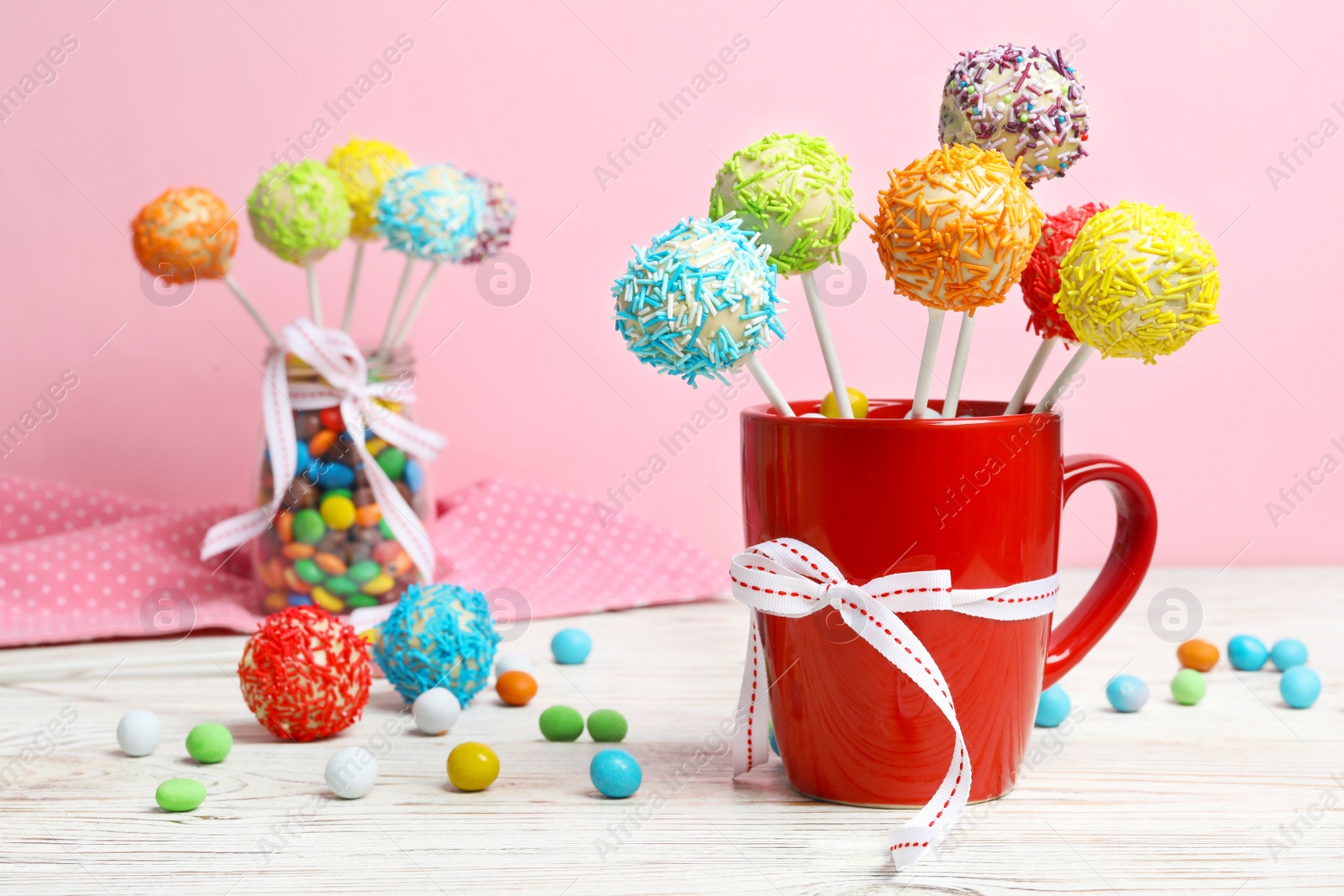 Photo of Cup with tasty cake pops on table, against pink background, space for text