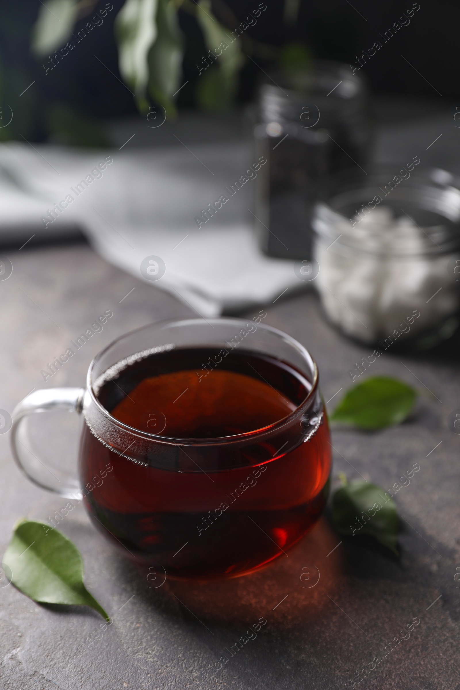 Photo of Tasty hot tea in cup and leaves on grey table, closeup