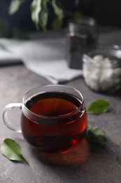 Tasty hot tea in cup and leaves on grey table, closeup