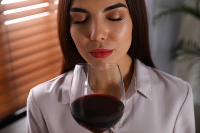 Photo of Beautiful young woman with glass of luxury red wine indoors, closeup view