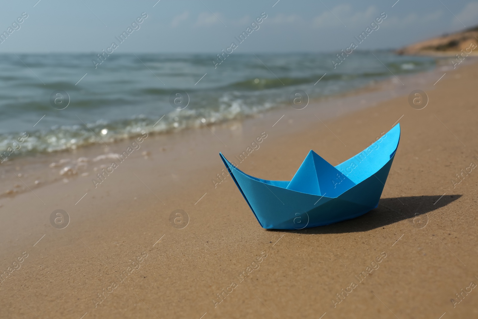 Photo of Blue paper boat on sandy beach near sea, space for text