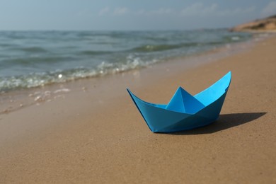 Blue paper boat on sandy beach near sea, space for text