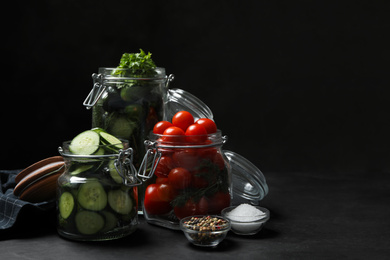 Photo of Pickling jars with fresh ripe vegetables and spices on black table. Space for text