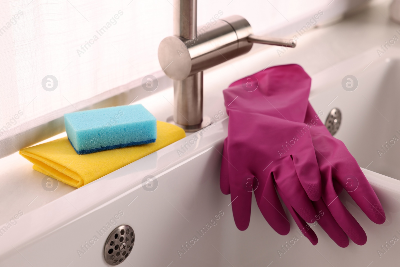 Photo of Sponge, rag and rubber gloves on kitchen sink indoors